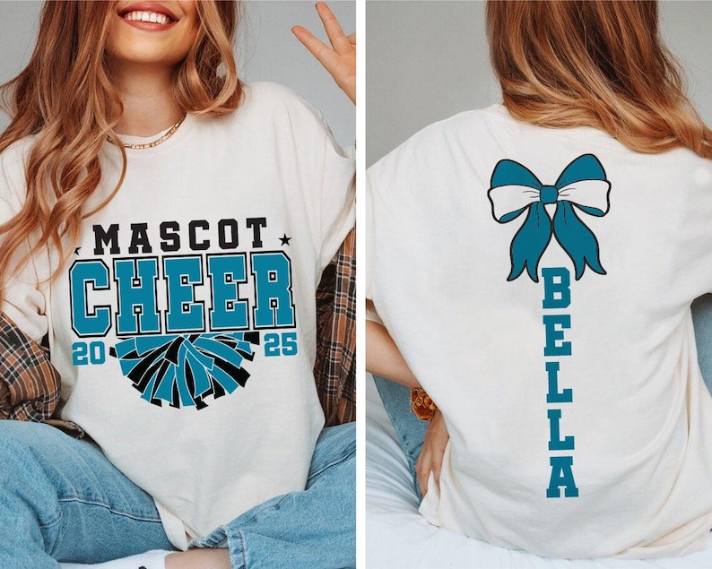 May include: White t-shirt with a blue and black cheerleading pom-pom graphic and the text "Mascot Cheer 20 25". The back of the shirt has a blue bow and the text "Bella" vertically down the back.