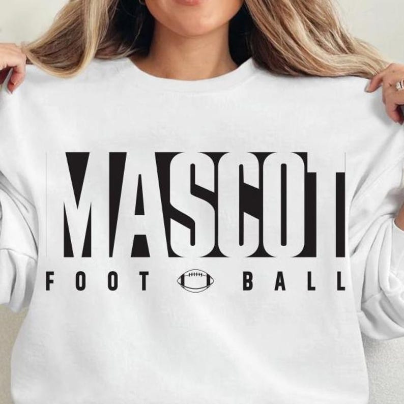 May include: White sweatshirt with the word "MASCOT" in bold, black, block letters. Below the word "MASCOT" is the text "FOOT BALL" with a football graphic in between. The sweatshirt is a crew neck.