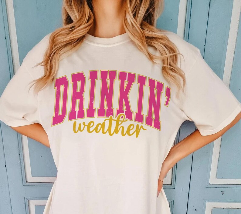May include: White t-shirt with pink and gold lettering that reads "Drinkin' weather".
