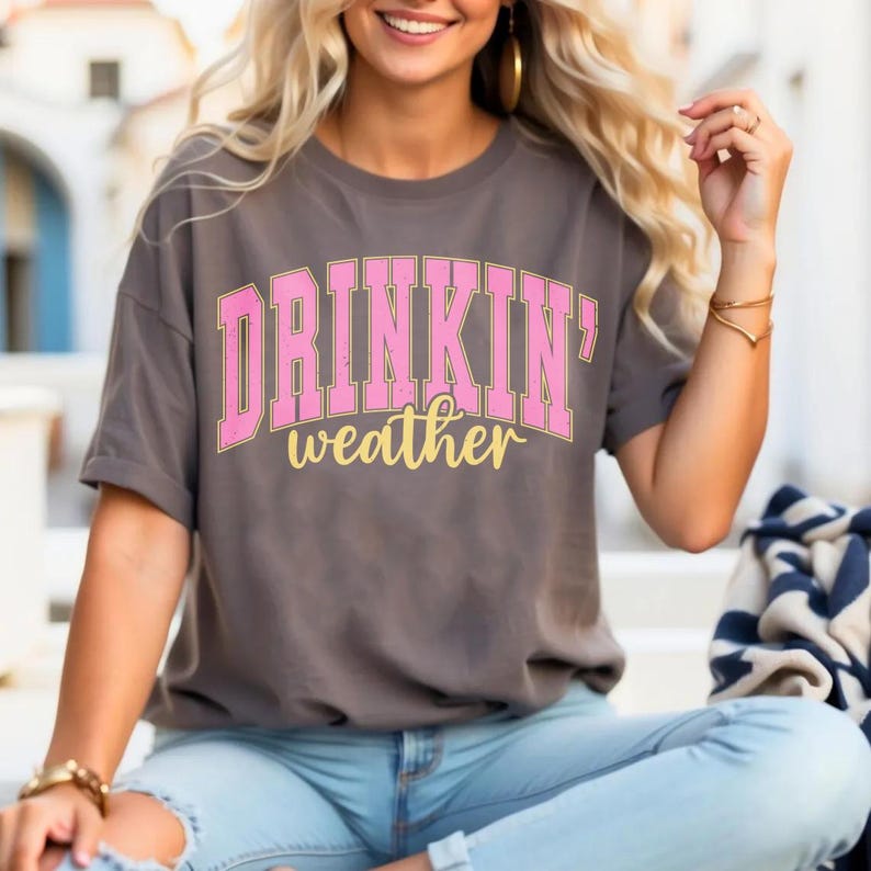 May include: A gray t-shirt with the text "DRINKIN' weather" in pink and yellow letters.