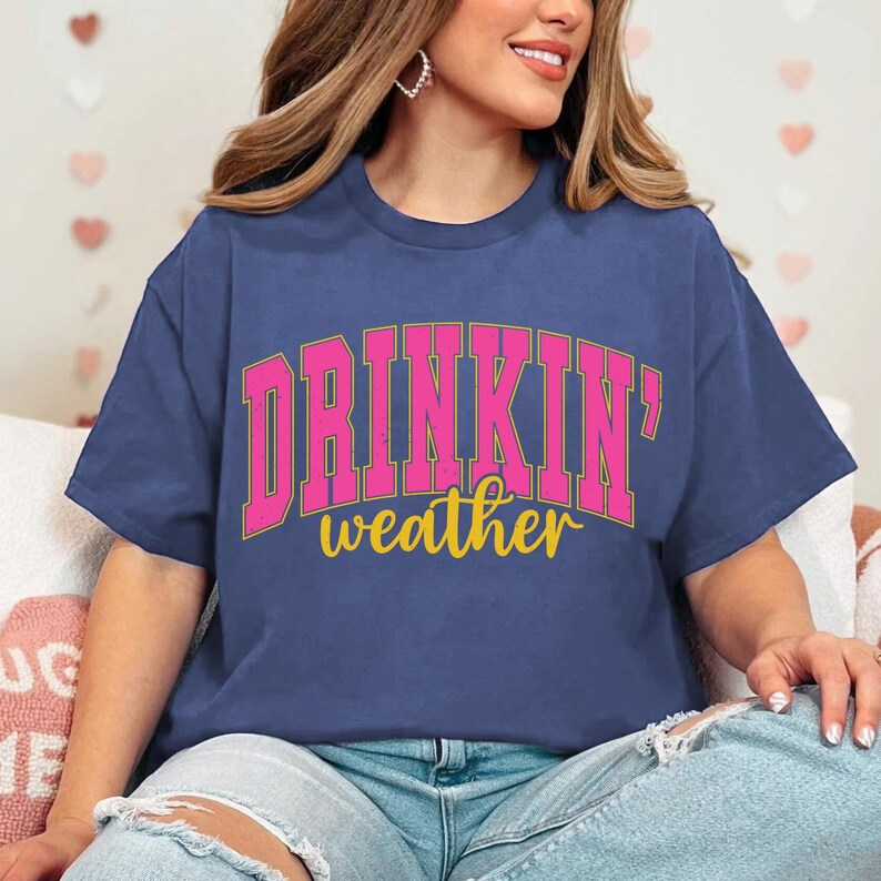May include: A blue t-shirt with a pink and gold graphic that says "Drinkin' weather".