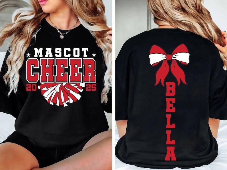 May include: Black cheerleading shirt with red and white pom-poms and the text "Mascot Cheer 2025". The back of the shirt has a red bow and the name "Bella" written vertically.