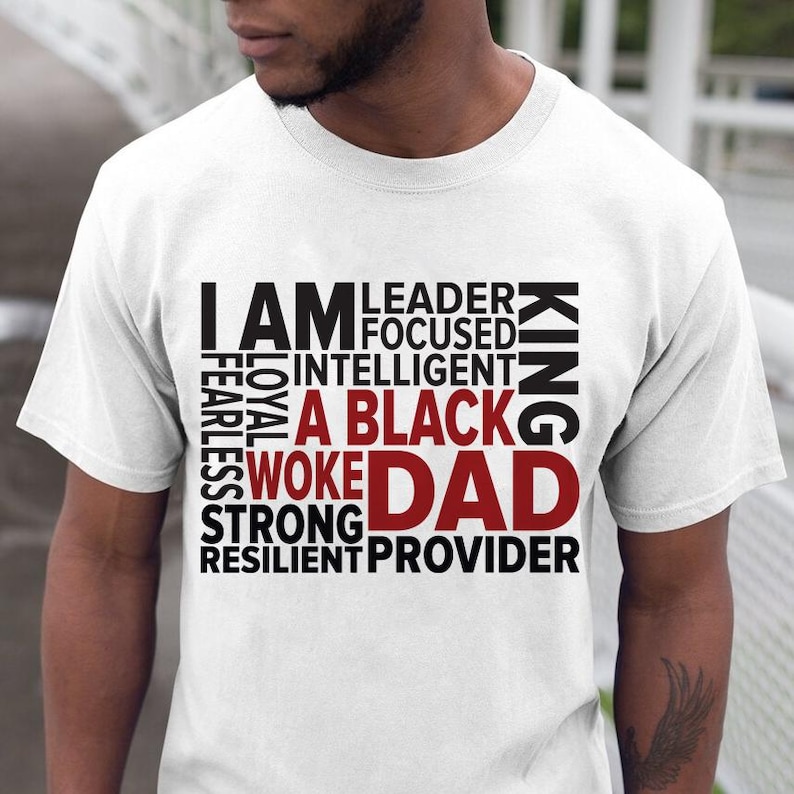 Op de afbeelding: Wit T-shirt met de tekst "I AM A BLACK WOKE DAD" in zwart en rood. Extra woorden zijn "Leader, Focused, Intelligent, King, Fearless, Loyal, Strong, Resilient, Provider."