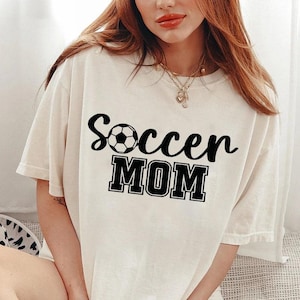 May include: White t-shirt with black text that says "Soccer Mom" and a black and white soccer ball graphic.