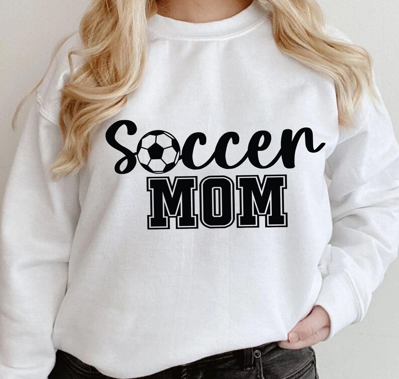 May include: White sweatshirt with black text that reads "Soccer Mom" and a black and white soccer ball graphic.