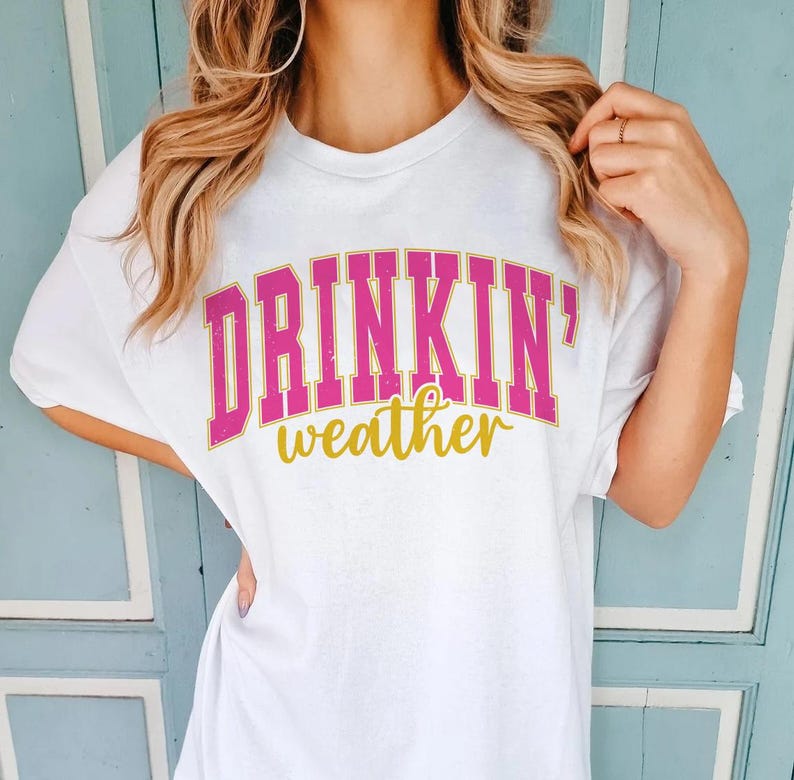 May include: White t-shirt with pink and gold lettering that reads "Drinkin' weather".