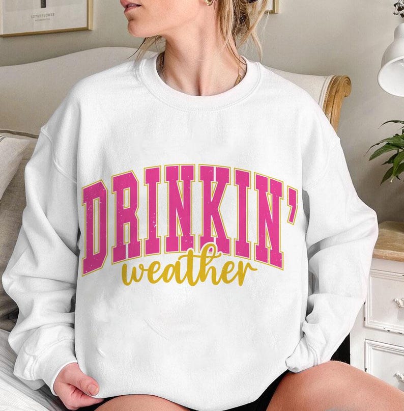 May include: White sweatshirt with the text "DRINKIN' weather" in pink and gold letters.