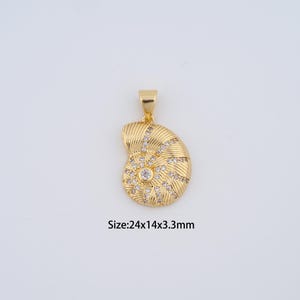 May include: A gold-colored pendant in the shape of a nautilus shell, adorned with small, clear gemstones. The pendant has a textured surface and a loop for a chain. The text on the image reads: Size: 24x14x3.3mm.