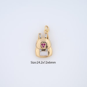 May include: A gold-colored backpack charm with a red heart-shaped gem and white accents. The charm has two straps with clear gems and a white rectangular gem at the bottom. The size is 24.2x12x6mm.