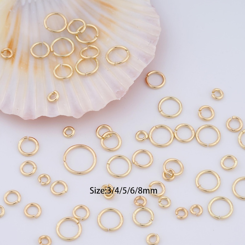 May include: Assortment of gold jump rings in various sizes, ranging from 3mm to 8mm. The jump rings are displayed on a white seashell background. Size: 3/4/5/6/8mm