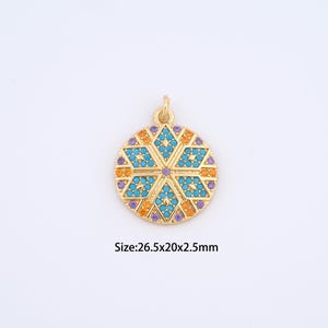 May include: Gold-toned pendant with a circular design. The pendant features a central turquoise pattern surrounded by orange and purple accents. The pendant measures approximately 1 inch in diameter and 0.1 inches thick.