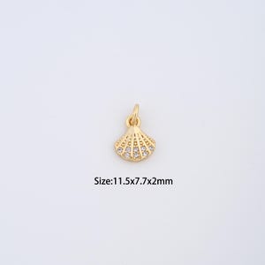 May include: A gold-colored seashell pendant with small, clear gemstones. The pendant has a loop at the top for a chain. The text "Size: 11.5x7.7x2mm" is below the pendant.