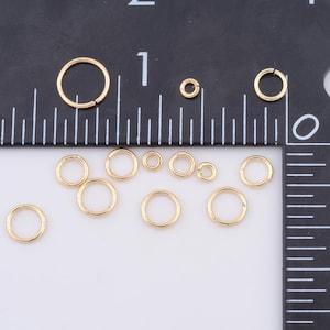 May include: A collection of gold jump rings of various sizes, displayed on a white surface with a ruler for scale.