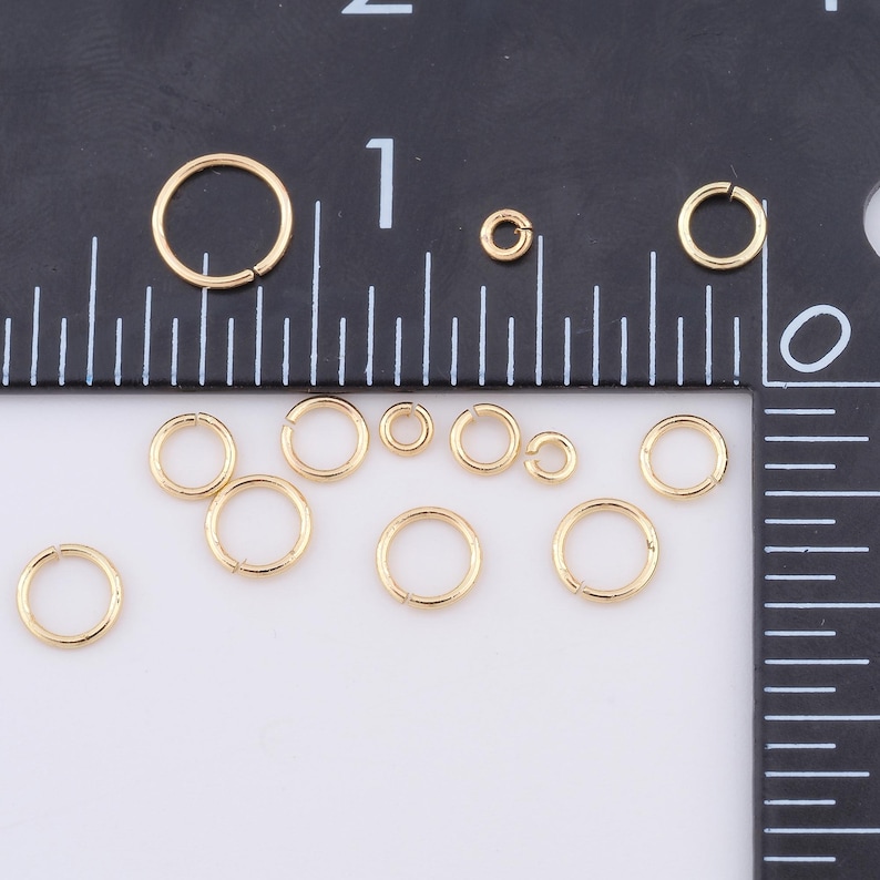 May include: A collection of gold jump rings of various sizes, displayed on a white surface with a ruler for scale.