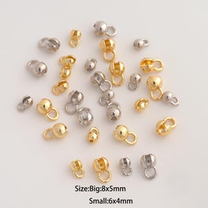 May include: A collection of gold and silver-toned metal crimp bead covers with attached loops, scattered across a plain surface. The text at the bottom indicates sizes of Big: 8x5mm and Small: 6x4mm for these jewelry making components.