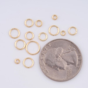 May include: A collection of 12 gold jump rings of various sizes, displayed next to a US quarter for scale.
