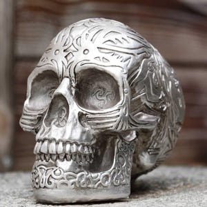 Può includere: Una scultura di teschio in argento con intricate incisioni dettagliate. Il teschio ha un design tribale ed è un oggetto decorativo per la casa.