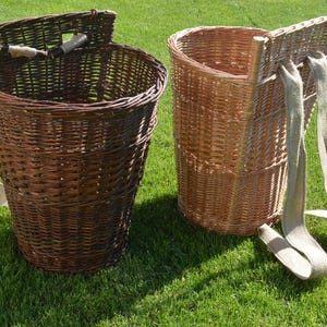 Może przedstawiać: Dwa wiklinowe kosze z paskami na ramiona na zielonej trawie. Jeden jest ciemnobrązowy, drugi jasnobrązowy. Oba mają cylindryczny kształt z klapą i uchwytem.