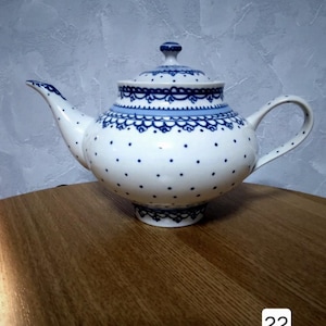 Könnte beinhalten: Eine weiße Teekanne mit einem blauen und weißen Tupfenmuster und einem blauen Spitzenmuster am oberen Rand. Die Teekanne hat einen Deckel und einen Henkel.