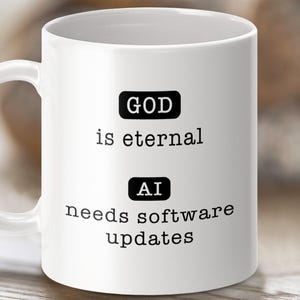 Może przedstawiać: Biały kubek ceramiczny z czarnym tekstem, który brzmi "GOD is eternal AI needs software updates".