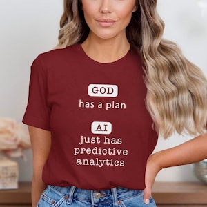 May include: A maroon t-shirt with white text that reads "GOD has a plan" and "AI just has predictive analytics".