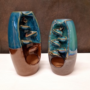 Op de afbeelding: Twee keramische wierookbranders met een blauwe en bruine glazuur. De branders hebben een uniek ontwerp met een waterval-effect.