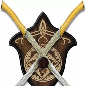 Peut inclure: Deux épées croisées avec des lames incurvées et des manches jaunes, montées sur un bouclier en bois. Le bouclier est brun foncé avec un motif décoratif brun clair et une bordure noire. Les épées sont argentées avec des motifs.