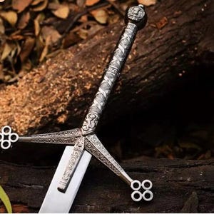 May include: A close-up of a silver sword with an ornate handle and crossguard. The blade is straight and polished, reflecting light. The handle features intricate patterns and a pommel. The sword rests on a dark wooden surface.