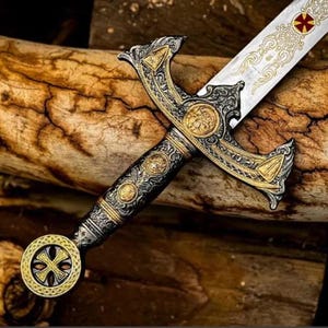 May include: An ornate sword with a silver blade and gold and black hilt. The blade features decorative etching and a red and gold emblem. The hilt has intricate gold detailing and a circular pommel with a cross design.