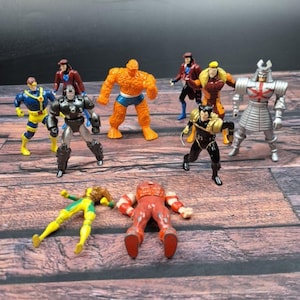 May include: A selection of colourful action figures depicting various superhero characters. The figures include a metallic silver robot, a muscular orange figure, and others in dynamic poses, showcasing a range of vibrant colours and designs.