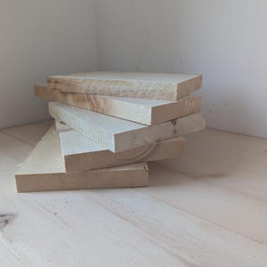 May include: A stack of five unfinished wooden boards, likely for crafting or woodworking projects.
