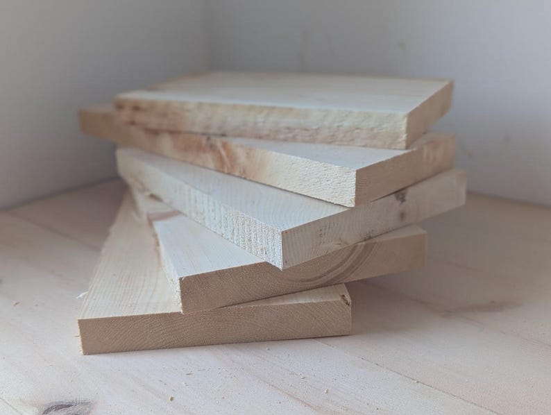 May include: A stack of five unfinished wooden boards, likely pine, with a natural wood grain. The boards are stacked on a light wood surface.