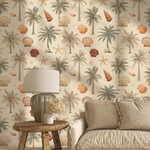 May include: A coastal-themed interior featuring a wallpaper with a repeating pattern of palm trees, seashells, and starfish in muted tones. A wooden side table holds a lamp and a vase of dried flowers, with a beige sofa in the foreground.