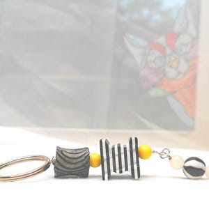 Genial llavero en blanco y negro con un toque de amarillo. Interesante llavero o dije para bolso o cartera.