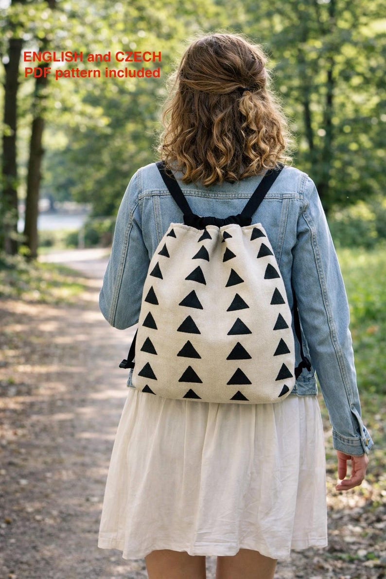 Puede incluir: Una mochila con cord&oacute;n de color crema con un patr&oacute;n repetido de tri&aacute;ngulos negros. La mochila tiene correas negras y se lleva sobre una chaqueta vaquera y un vestido blanco. El texto "ENGLISH and CZECH PDF pattern included" es visible.