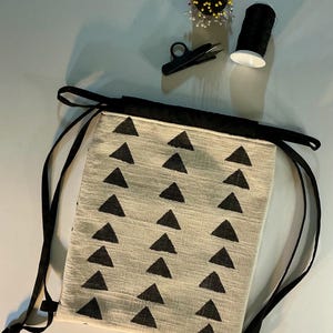 Puede incluir: Una bolsa beige con cord&oacute;n y un patr&oacute;n de tri&aacute;ngulos negros, ribete negro y cordones negros. Los suministros de costura incluyen un alfiletero negro, hilo negro y tijeras peque&ntilde;as negras.