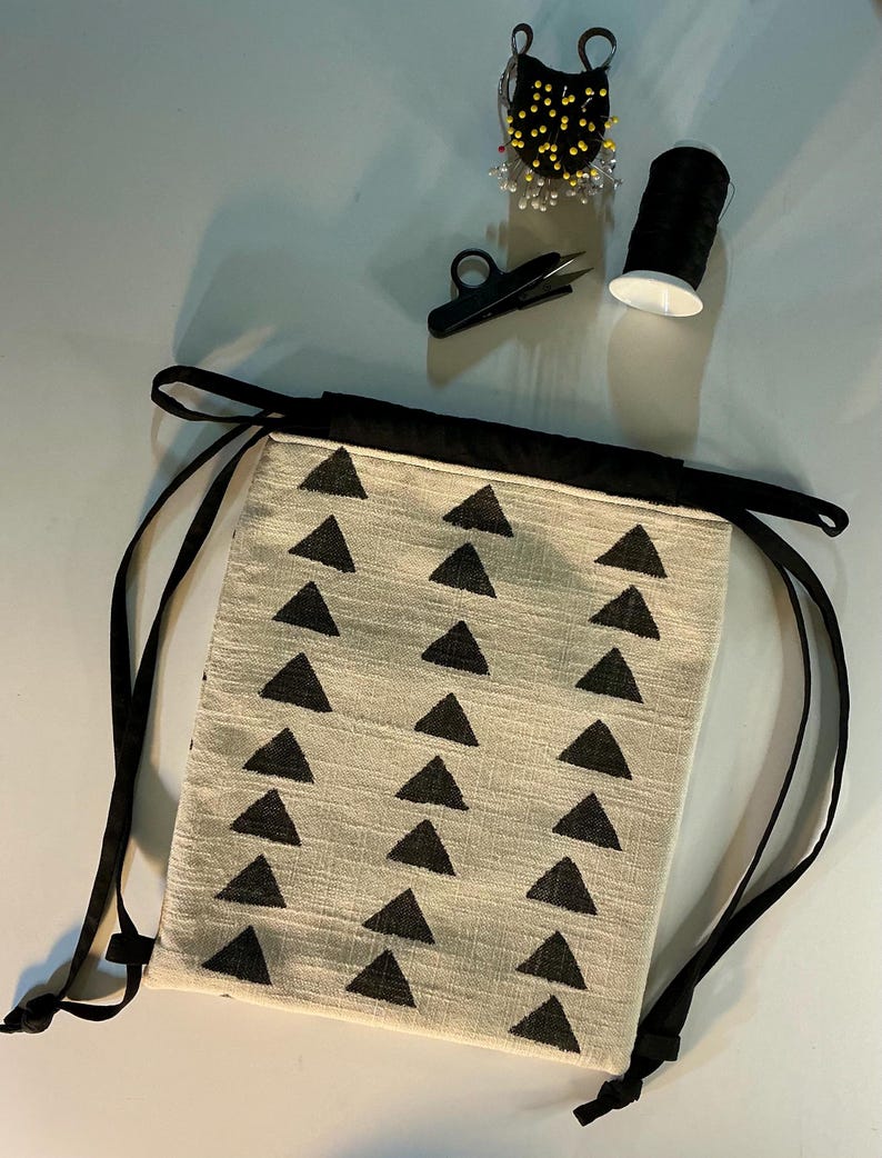 Puede incluir: Una bolsa beige con cord&oacute;n y un patr&oacute;n de tri&aacute;ngulos negros, ribete negro y cordones negros. Los suministros de costura incluyen un alfiletero negro, hilo negro y tijeras peque&ntilde;as negras.