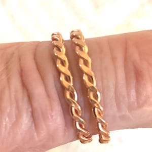 Peut inclure: Deux bagues fines de couleur or rose présentant une texture torsadée semblable à une corde. Les anneaux ont une finition métallique polie et un motif en spirale continu qui fait le tour de chaque bague, créant un aspect uniforme.