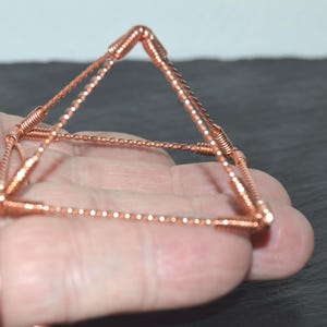 Puede incluir: Una escultura en forma de pir&aacute;mide construida con alambre de cobre. La estructura presenta cuatro bordes de base y cuatro bordes inclinados que se encuentran en un punto superior, todos hechos de segmentos de alambre de cobre trenzado unidos por juntas de alambre en espiral.