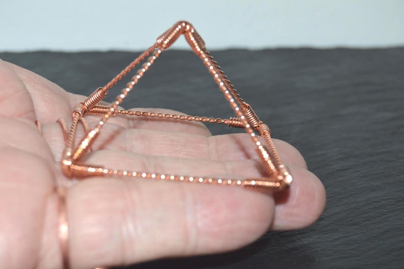 Puede incluir: Una escultura en forma de pir&aacute;mide construida con alambre de cobre. La estructura presenta cuatro bordes de base y cuatro bordes inclinados que se encuentran en un punto superior, todos hechos de segmentos de alambre de cobre trenzado unidos por juntas de alambre en espiral.