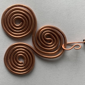 May include: A copper-colored pendant featuring three spiral designs connected by wire. The pendant is attached to a black cord with a copper clasp. The spirals are made of coiled wire.