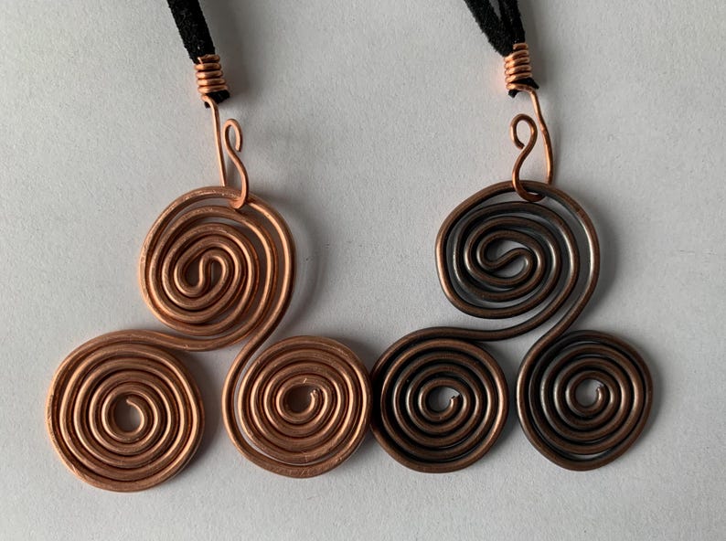May include: Two copper wire spiral pendants with black cords. One pendant is a bright copper color, and the other is a darker, oxidized copper. Each pendant features three connected spirals, with a loop at the top for the cord.