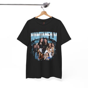 Könnte beinhalten: Schwarzes T-Shirt mit einem blauen Grafikdesign mit dem Text "NAMTANFILM" über einer Gruppe von Personen. Das Design hat eine Vintage-Ästhetik. Das T-Shirt hängt an einem Kleiderbügel.