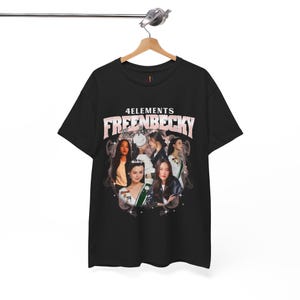 May include: Black t-shirt with a graphic design featuring the text "4ELEMENTS FREENBECKY The Air" in pink and white. The design includes images of several women. The t-shirt is displayed on a wooden hanger.