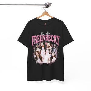 May include: Black t-shirt with a pink graphic reading "The Air FREENBECKY" above a collage of women's portraits. The design has a vintage, distressed appearance. The t-shirt is displayed on a wooden hanger.