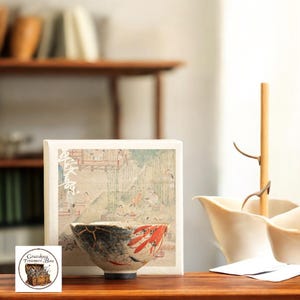 Pode incluir: Uma tigela de cerâmica com um design único, apresentando reparo kintsugi preto e dourado e detalhes em vermelho. A tigela é colocada em frente a uma caixa com uma ilustração de estilo japonês. A imagem também inclui um elemento decorativo de madeira e um pequeno logotipo.