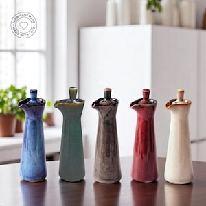 May include: Five ceramic oil and vinegar bottles in different colours. The bottles are all the same shape, with a narrow neck and a wide base. The colours are blue, green, grey, red, and white.