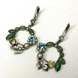Puede incluir: Un par de pendientes plateados con un diseño floral y de hojas. Cada pendiente presenta una flor de piedra preciosa azul claro, piedras preciosas verdes y amarillas y pequeñas perlas blancas. Cierre de palanca.