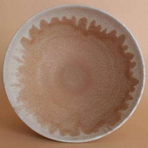 Könnte beinhalten: Eine große, runde Keramikschüssel mit weißer Glasur und braunem, gesprenkeltem Design. Die Schüssel hat einen breiten Rand und einen leicht gewölbten Boden.