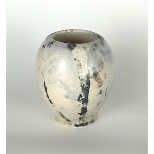 May include: A ceramic vase with a rounded body and a wide opening. The vase is primarily off-white with dark gray and black streaks and patches. The base is slightly darker than the body. The interior is a light tan color.